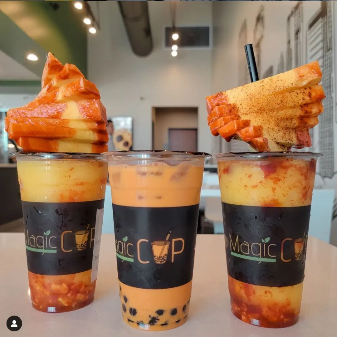 Three layered drinks with fried chicken pieces on top, served in branded cups at a counter