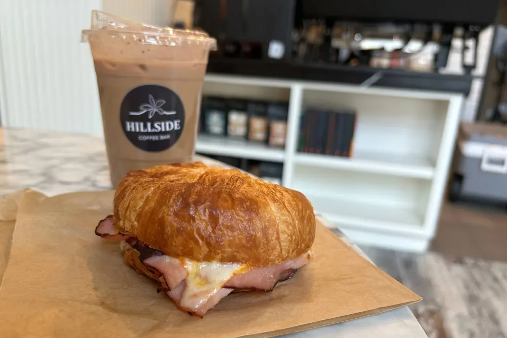 Croissant sandwich with ham and cheese beside iced coffee drink on counter