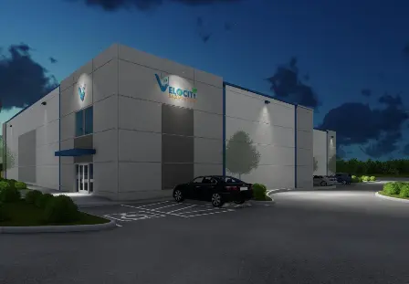 Modern white badminton facility with large windows and parked car at dusk