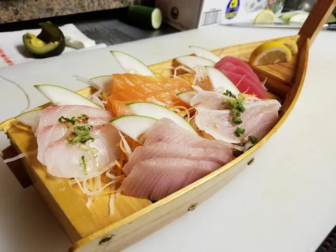 Assorted raw fish slices including salmon and tuna arranged on a wooden boat-shaped plate with garnish and daikon radish