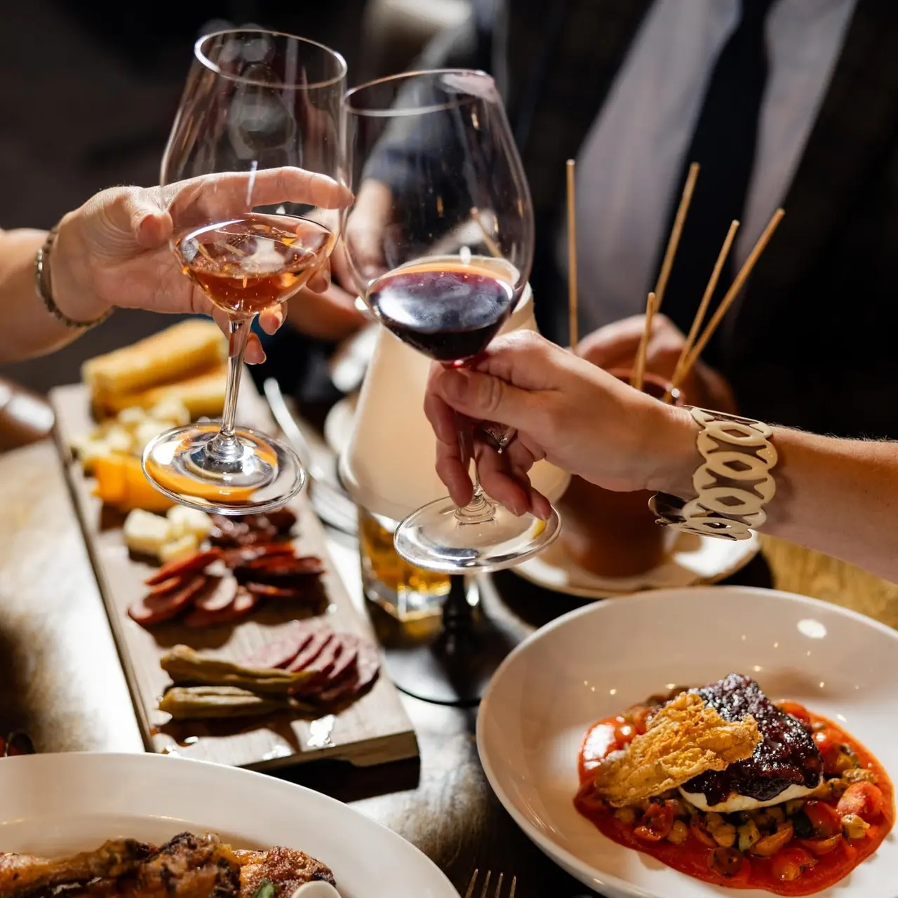 hands toasting with wine glasses and food on the table