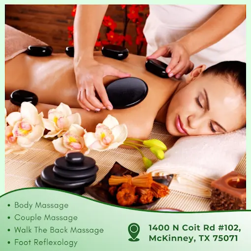 Woman receiving hot stone massage on back with therapist's hands applying black stones, flowers and dried herbs arranged nearby