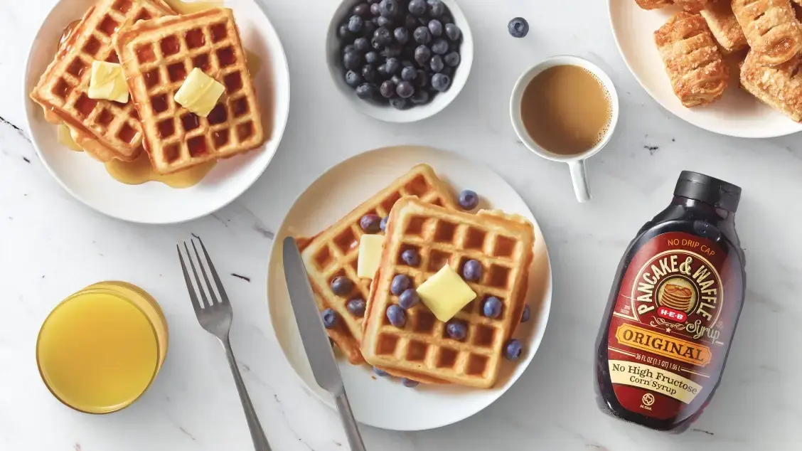 Overhead view of waffles topped with blueberries and butter, served with orange juice, coffee, croissants, and syrup bottle