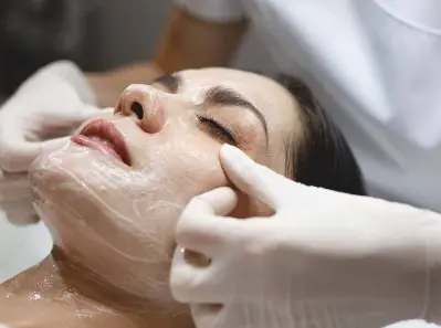Aesthetician applying a creamy face mask to a client's face during a spa treatment