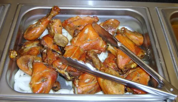 Roasted chicken pieces in a metal serving tray with tongs
