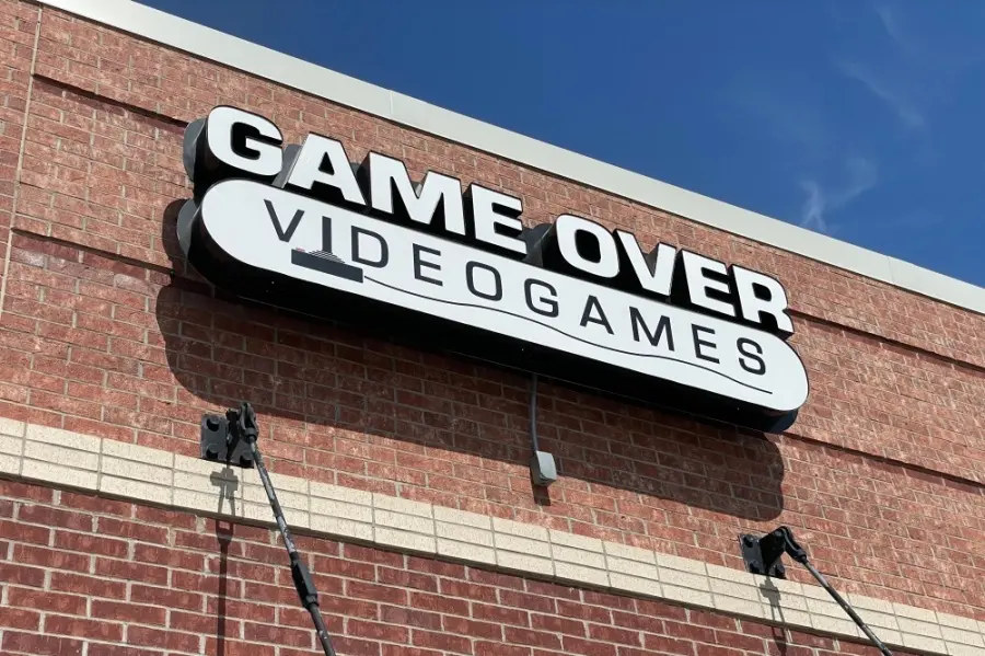 White signage reading "Game Over Videogames" mounted on brick storefront against blue sky