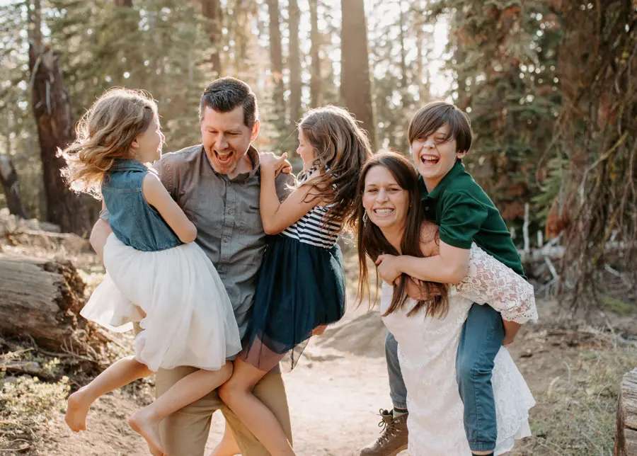 Family of five laughing together on a forest path surrounded by tall trees
