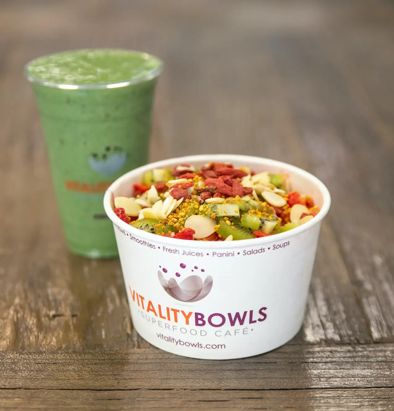 Acai bowl topped with granola, berries, and nuts beside a green smoothie on wooden surface