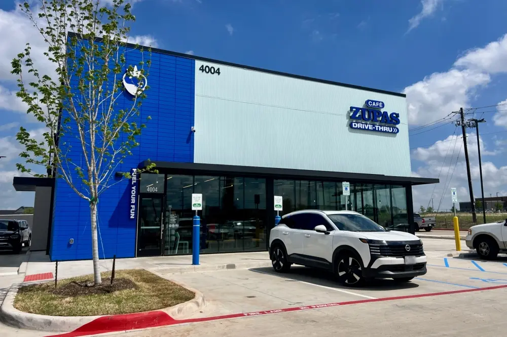 Modern restaurant exterior with blue and white facade, white SUV parked in front, young tree, and clear sky