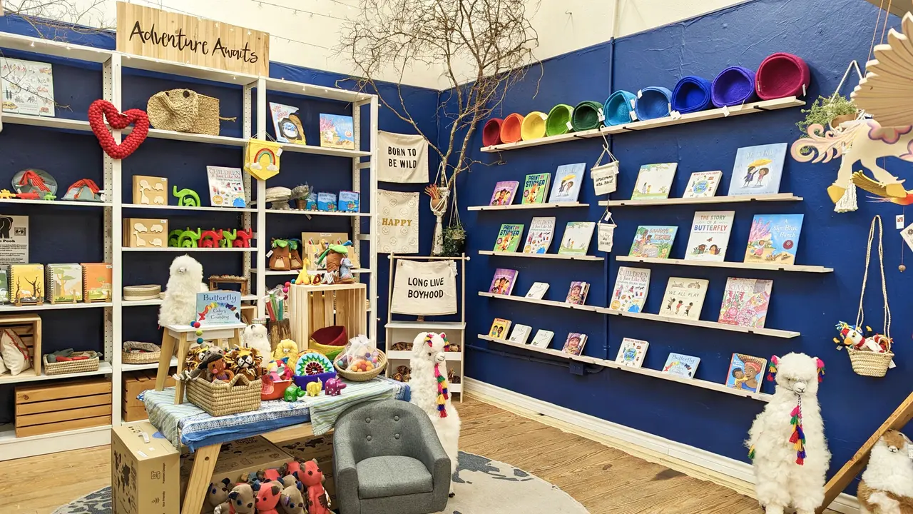 Retail shop interior with blue walls displaying colorful bowls on shelves, books, handmade goods, and decorative items on wooden shelving units