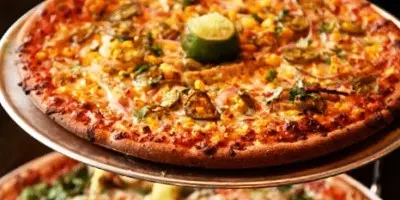 Whole pizza with melted cheese, tomato sauce, and toppings including jalapeño slices on white plate