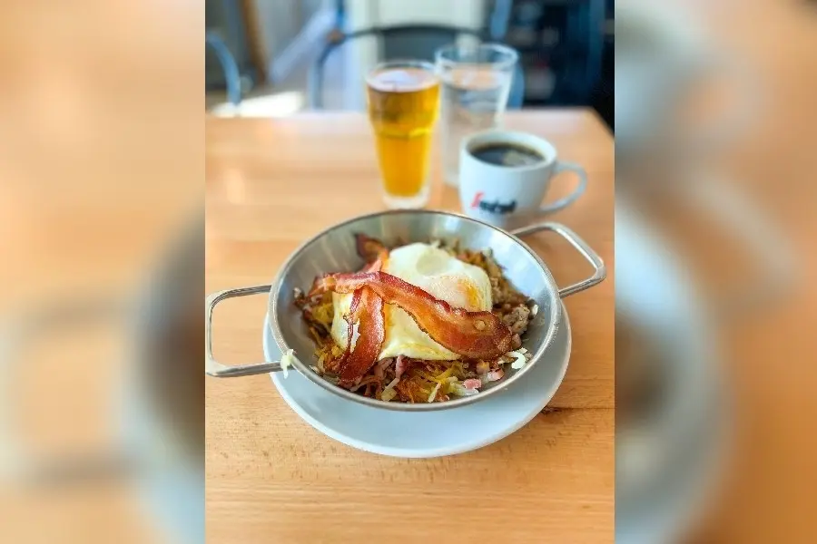 Skillet with bacon, eggs, and hash browns, served with orange juice and coffee on wooden table