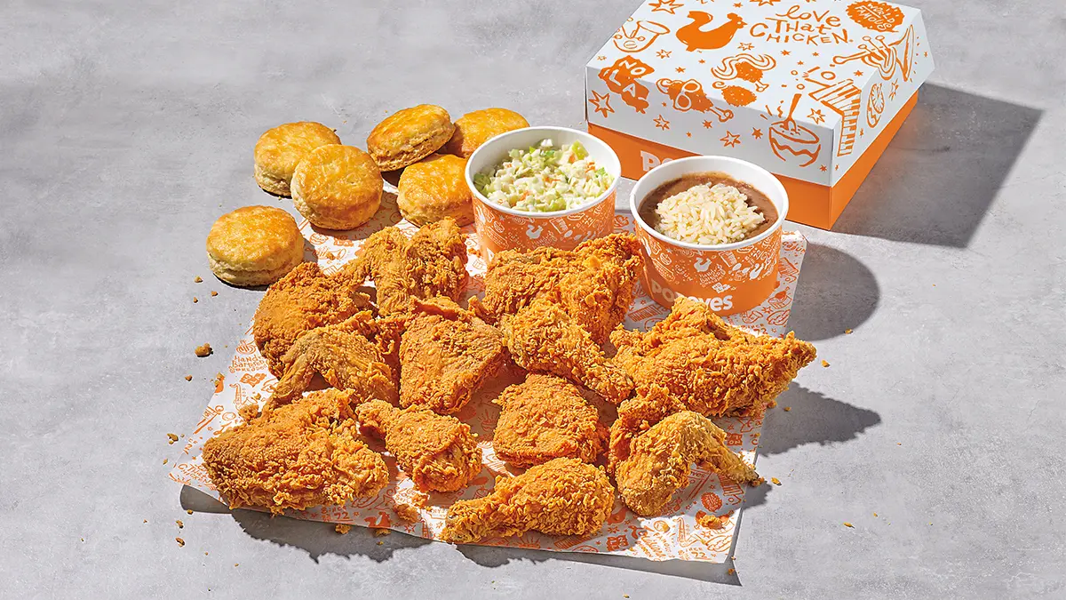 Golden fried chicken pieces, biscuits, and side dishes arranged on packaging against a light background