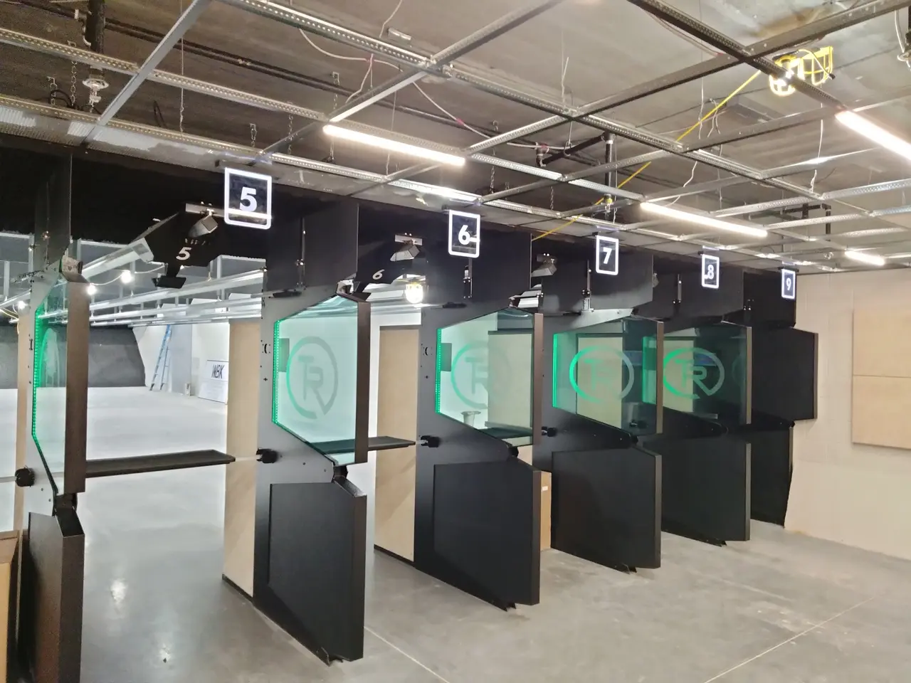 Row of indoor shooting range stalls with numbered targets and green bullseyes on black dividers