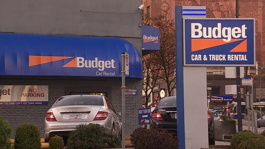 Budget Car & Truck Rental storefront with signage and parked white sedan on urban street
