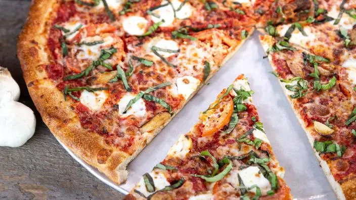 NY-style pizza with tomato sauce, melted cheese, fresh basil, and sliced garlic, one slice on parchment paper