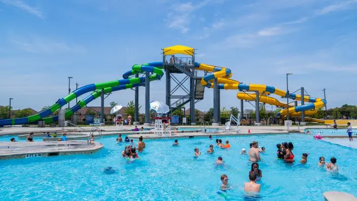 Crowded outdoor swimming pool with colorful water slides and tower features under blue sky
