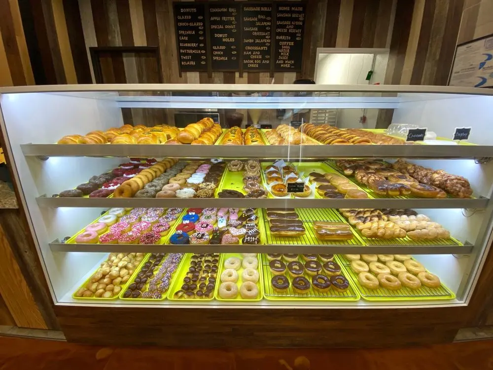 Illuminated display case with four shelves holding assorted donuts and pastries in colorful green trays