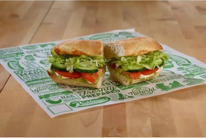 Two halves of a sandwich with lettuce and tomato on a printed wrapper, on wooden surface