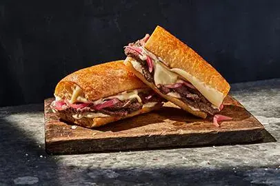 Toasted sandwich halves with melted cheese and cured meat on wooden board