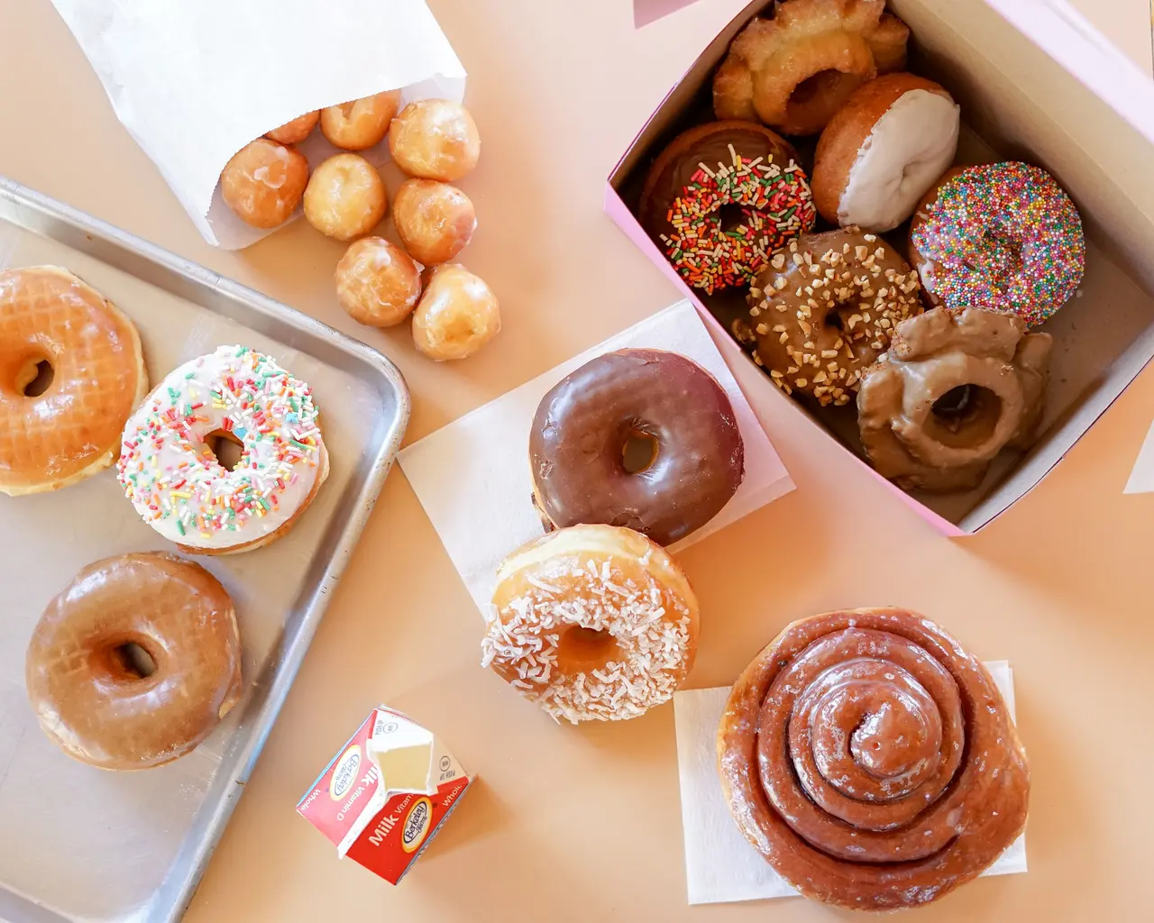 Assorted donuts including glazed, chocolate, sprinkled, and cinnamon swirl varieties in boxes and on plates