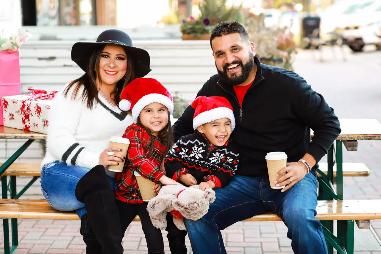 Family sitting on a table outside with coffee cups in hand and festive holiday gear on