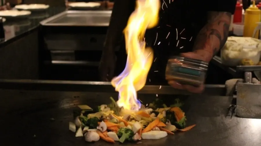 Chef flaming vegetables on a hibachi griddle in front of diners