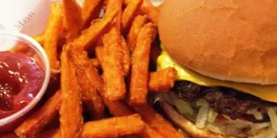 Burger with lettuce and tomato alongside sweet potato fries and red dipping sauce