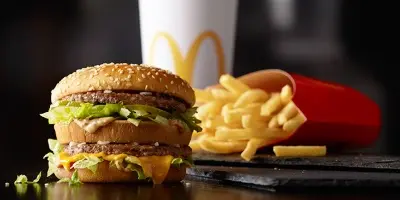 Double cheeseburger with lettuce, fries in red container, and beverage in background on dark surface