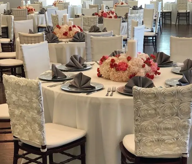 Banquet room with round tables dressed in cream linens, gray folded napkins, and red and pink floral centerpieces