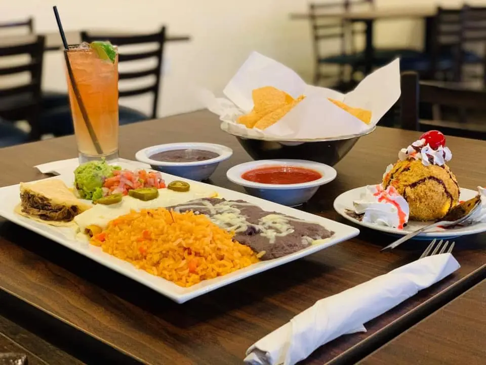 Plated Mexican food with rice, beans, and tacos alongside chips, salsa, and a drink on a restaurant table