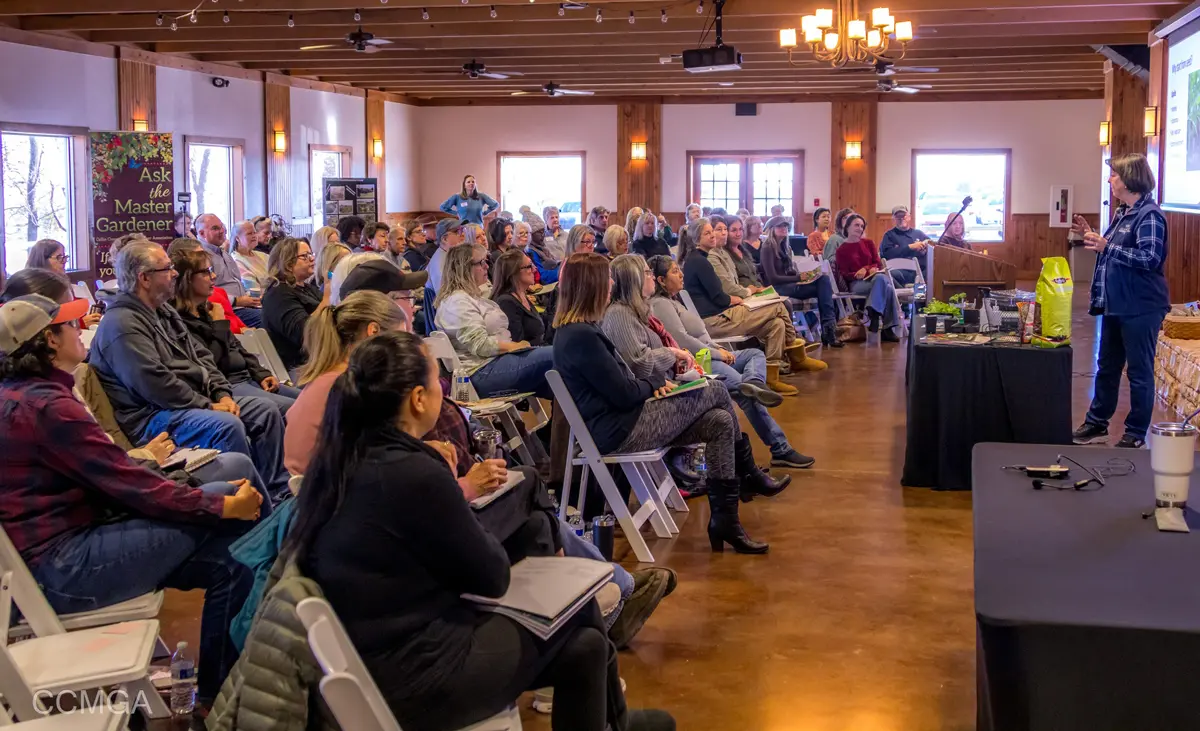 Large group of people seated in rows facing a speaker during an indoor workshop presentation with wooden ceiling and warm lighting