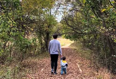 Adult and child walking together on a woodland path covered with fallen leaves