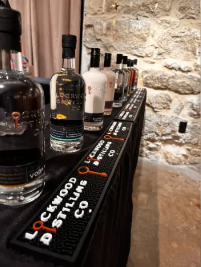Row of spirit bottles displayed on black shelf against stone wall, with cream curtain visible behind
