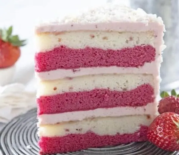 Layered cake with alternating pink and vanilla frosting and white frosting on top, garnished with fresh strawberries on the side