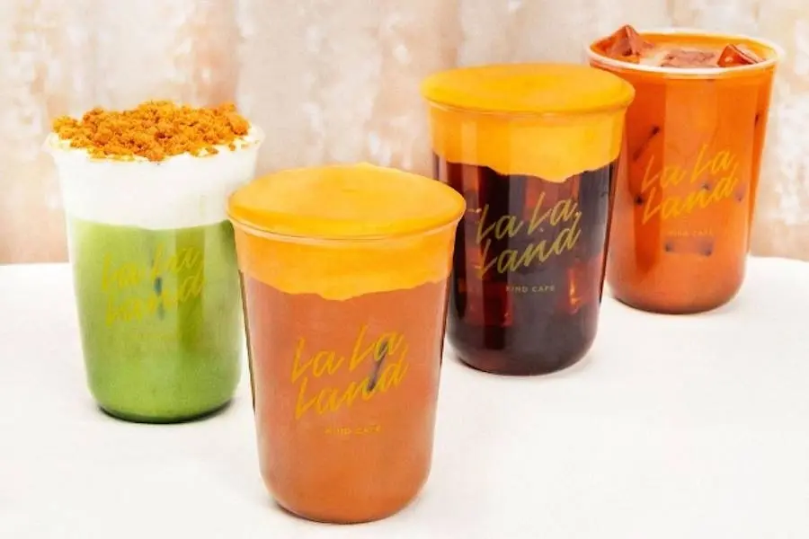 Four colorful takeaway drinks with sealed lids in a row, including green, amber, and dark beverages with golden toppings