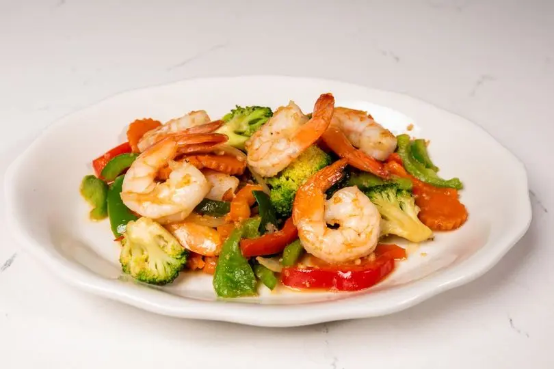 Cooked shrimp with broccoli, red peppers, and green onions on a white plate