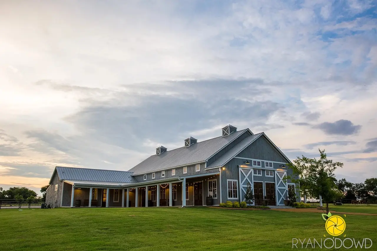 Large modern barn with covered porch and X-pattern doors on green pasture under cloudy sky