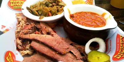 Sliced brisket, pulled pork, beans, and fried sides on white plates with onion and pickle