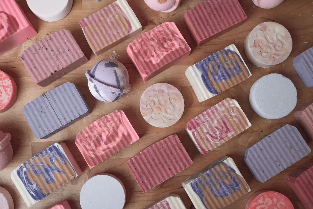 Assorted handmade soaps with striped wrappers in pink, blue, and cream, arranged with circular soap bars on wooden surface