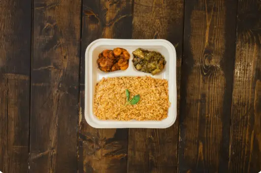 Compartmented takeout tray with rice, roasted vegetables, and potatoes on dark wooden surface
