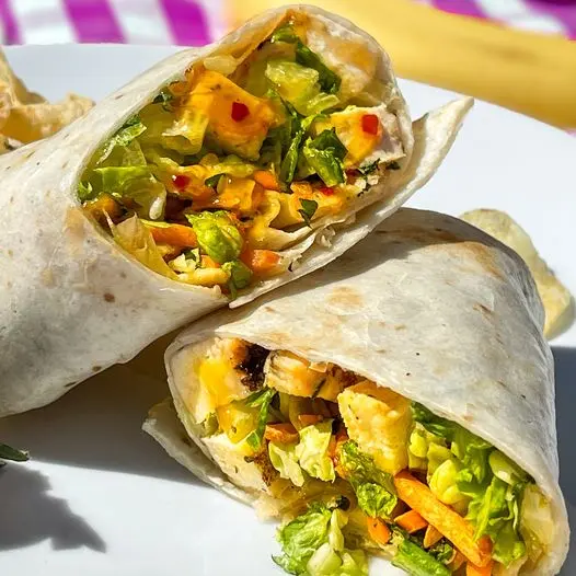 Two wraps filled with grilled chicken, lettuce, bell peppers, and other fresh vegetables on a white plate