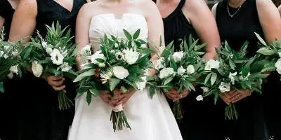 Bride in white dress and bridesmaids in black holding white and green flower bouquets