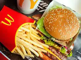Hamburger with lettuce and tomato on sesame seed bun, golden french fries in red container, and soft drink with straw