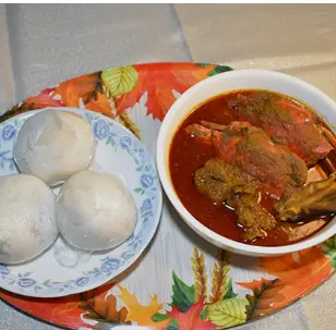 Three steamed white dumplings on decorative plate beside bowl of red stew with meat and vegetables on patterned tablecloth