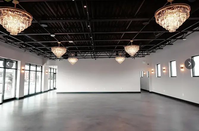 Empty event space with polished concrete floor, crystal chandeliers, black ceiling, and large windows along one wall