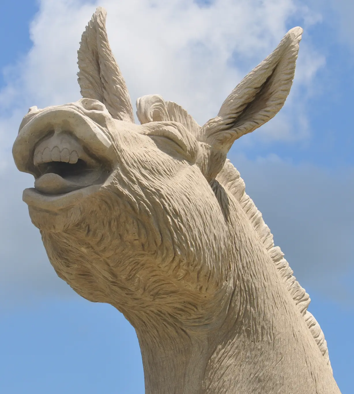 Carved wooden statue of a goat's head with upright ears against blue sky and clouds