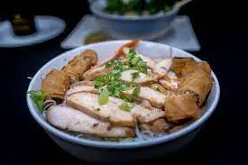 Sliced poached chicken with crispy fried shallots and fresh herbs on a white plate