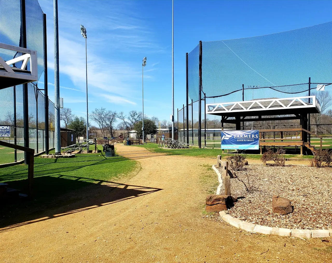 Baseball practice facility with multiple batting cages, infield dirt, and tall netting under clear blue sky