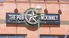 Illuminated pub sign with star logo mounted on brick building exterior, hanging pendant lights above